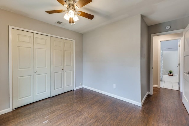 unfurnished bedroom featuring visible vents, a closet, baseboards, and dark wood-style flooring