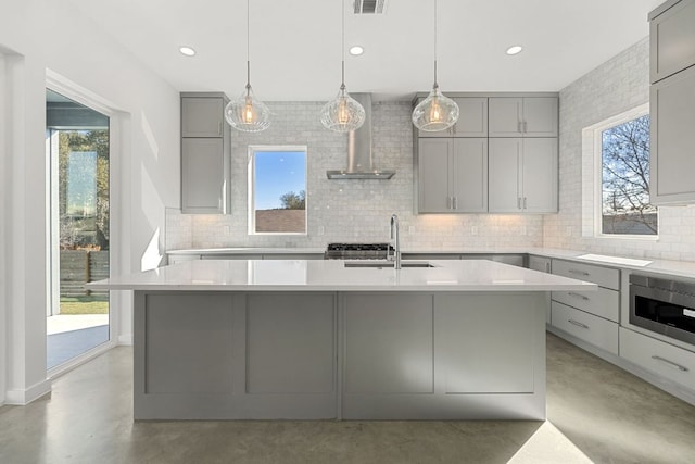 kitchen featuring gray cabinetry, a sink, finished concrete flooring, wall chimney range hood, and stainless steel microwave