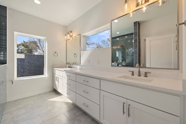 bathroom featuring double vanity, walk in shower, a sink, and baseboards