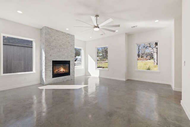 unfurnished living room featuring recessed lighting, finished concrete floors, ceiling fan, a stone fireplace, and baseboards