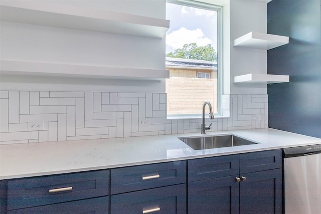 kitchen with blue cabinetry, open shelves, backsplash, stainless steel dishwasher, and a sink