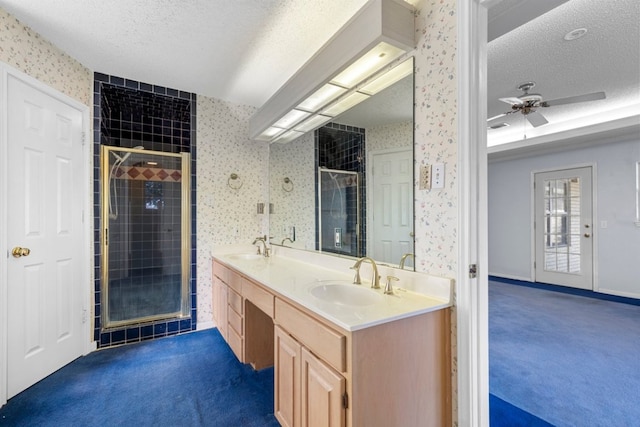 full bathroom with a textured ceiling, a sink, a shower stall, double vanity, and wallpapered walls