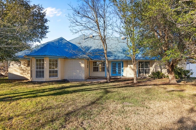 back of property featuring metal roof, a yard, french doors, and brick siding