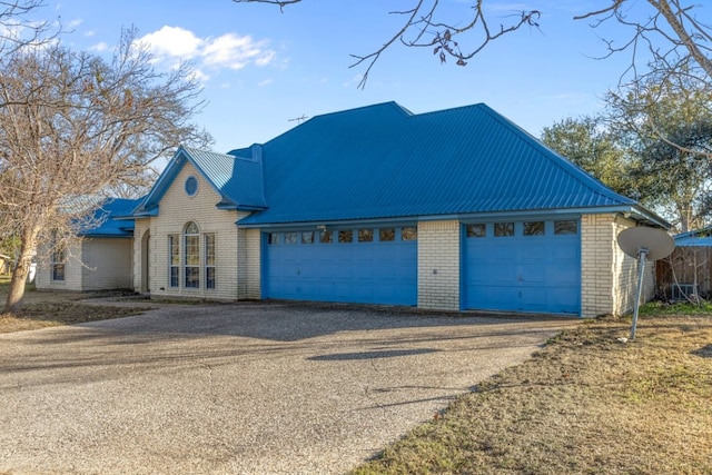 view of front of home with metal roof, driveway, brick siding, and a garage