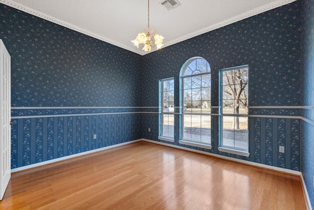 spare room featuring wood finished floors, visible vents, a notable chandelier, and wallpapered walls