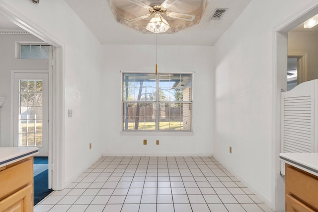 unfurnished dining area with light tile patterned flooring, visible vents, baseboards, a ceiling fan, and a tray ceiling