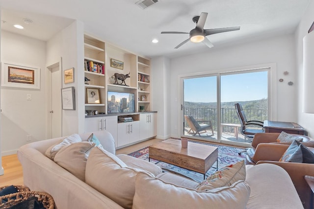 living area featuring built in features, visible vents, baseboards, light wood-style flooring, and ceiling fan