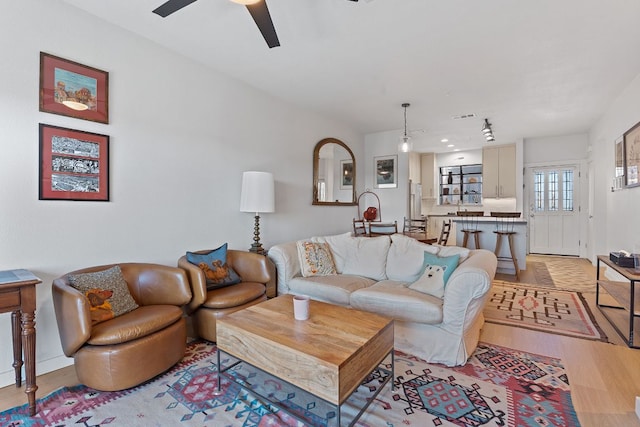 living room featuring baseboards, light wood-type flooring, visible vents, and a ceiling fan