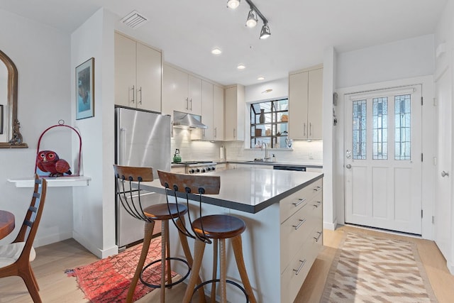 kitchen with visible vents, decorative backsplash, stove, under cabinet range hood, and a kitchen bar