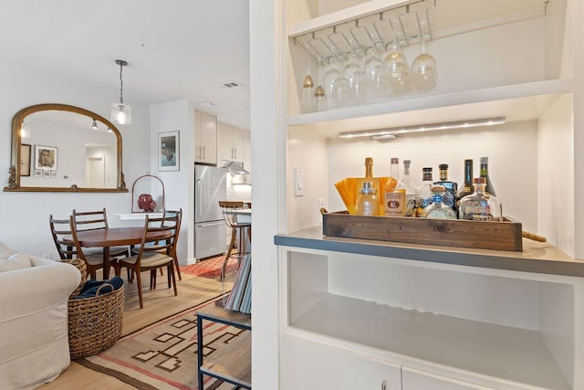 bar featuring visible vents, light wood-style flooring, freestanding refrigerator, hanging light fixtures, and under cabinet range hood