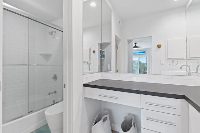 full bath with combined bath / shower with glass door, ceiling fan, vanity, and toilet