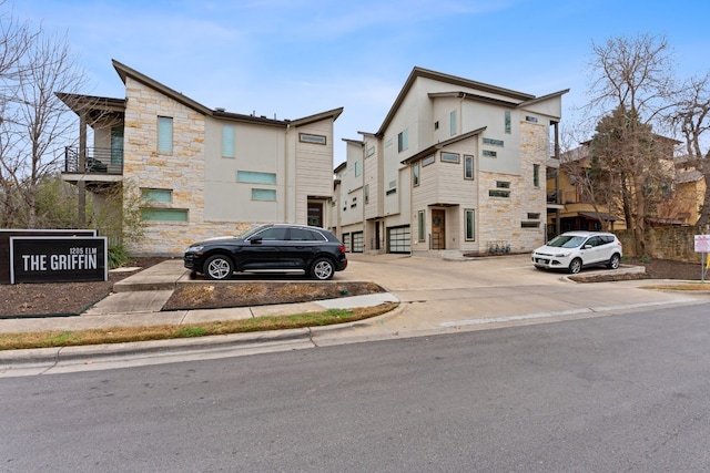 townhome / multi-family property with stone siding and uncovered parking