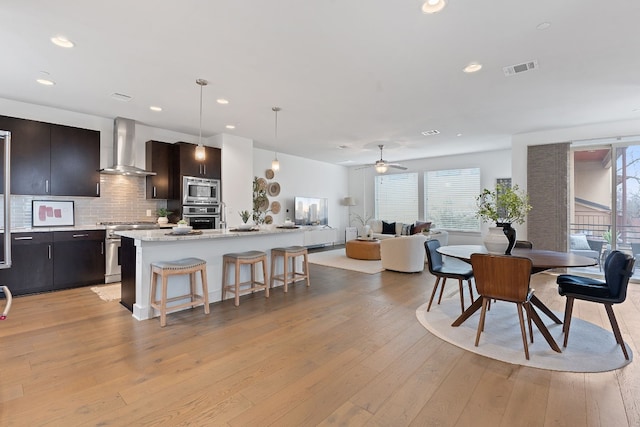 kitchen with stainless steel appliances, a kitchen breakfast bar, light wood-style floors, decorative backsplash, and wall chimney exhaust hood