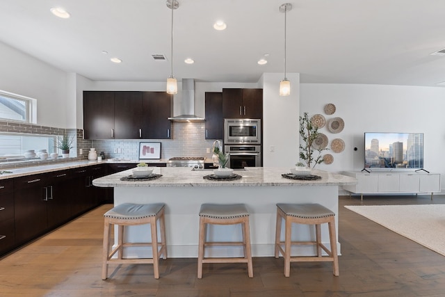 kitchen featuring wall chimney exhaust hood, visible vents, appliances with stainless steel finishes, and a kitchen breakfast bar