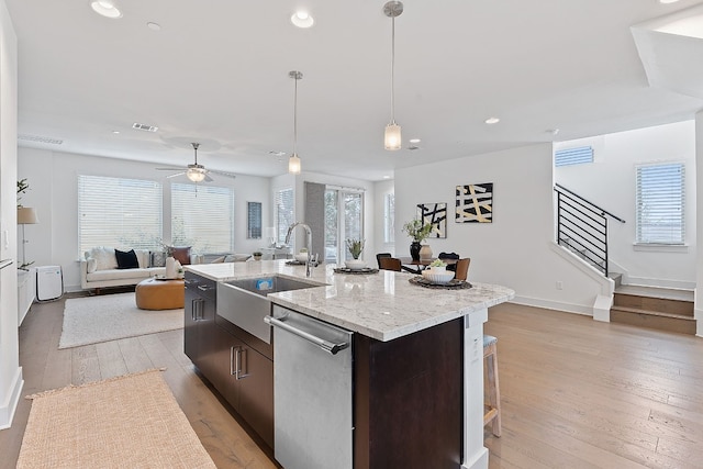 kitchen featuring stainless steel dishwasher, light wood-style floors, a sink, dark brown cabinets, and plenty of natural light