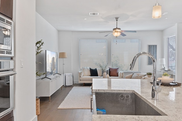 kitchen with light stone counters, visible vents, appliances with stainless steel finishes, a sink, and wood finished floors