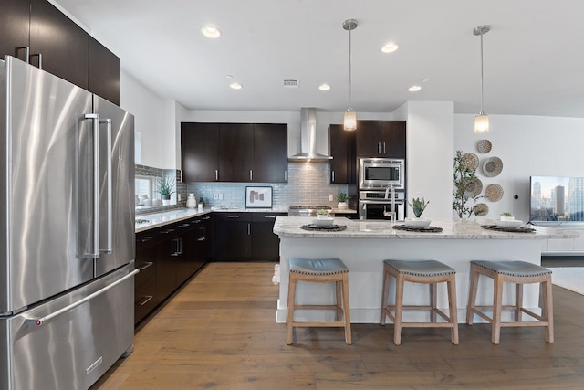 kitchen featuring tasteful backsplash, a kitchen breakfast bar, stainless steel appliances, light wood-type flooring, and wall chimney range hood