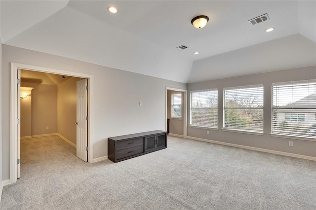 unfurnished room featuring baseboards, visible vents, vaulted ceiling, and light colored carpet