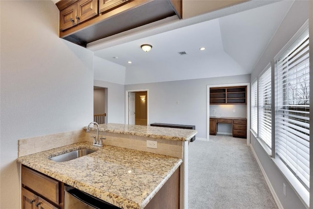 kitchen featuring a sink, vaulted ceiling, built in desk, and light colored carpet