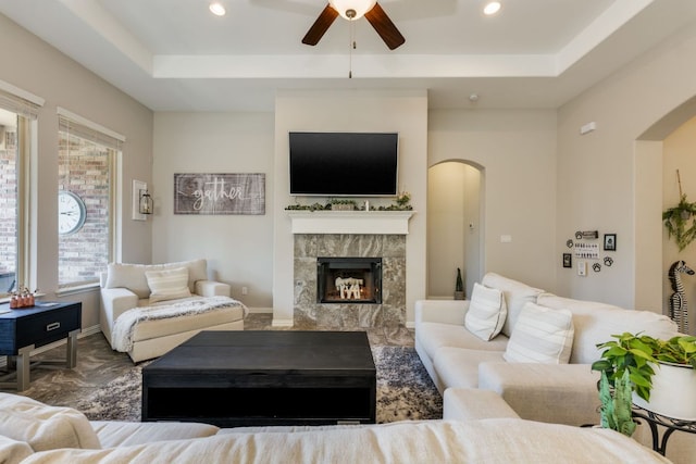 living area featuring arched walkways, a premium fireplace, a raised ceiling, and recessed lighting