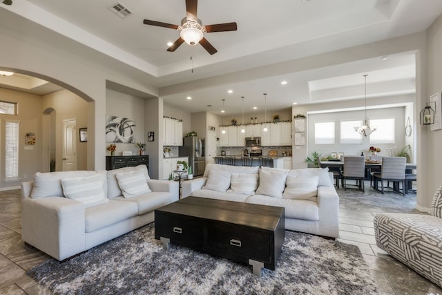 living area featuring a tray ceiling, arched walkways, recessed lighting, visible vents, and ceiling fan with notable chandelier