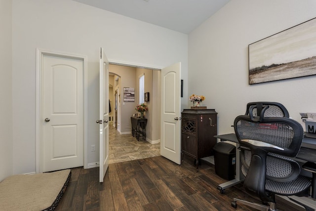 home office featuring arched walkways, dark wood-style flooring, and baseboards