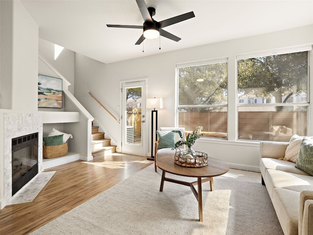 living area with stairway, a tiled fireplace, a ceiling fan, wood finished floors, and baseboards