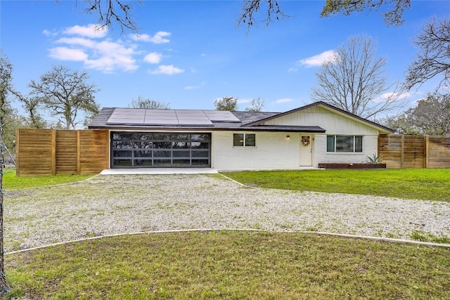 view of front facade featuring driveway, fence, solar panels, and a front yard