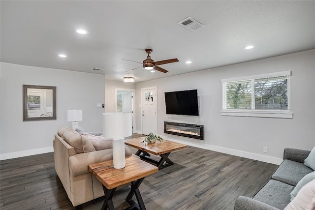 living room with dark wood-type flooring, a glass covered fireplace, visible vents, and baseboards