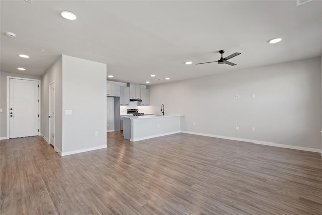 unfurnished living room with recessed lighting, a ceiling fan, a sink, wood finished floors, and baseboards