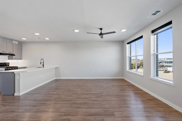 kitchen featuring baseboards, visible vents, under cabinet range hood, stainless steel range with gas cooktop, and a sink