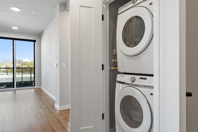 laundry area with recessed lighting, stacked washing maching and dryer, wood finished floors, laundry area, and baseboards