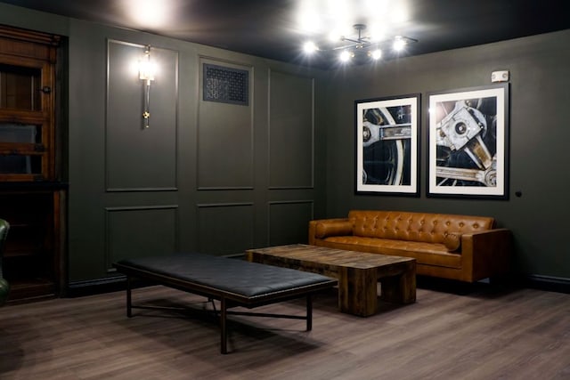 living area featuring an inviting chandelier, wood finished floors, and a decorative wall