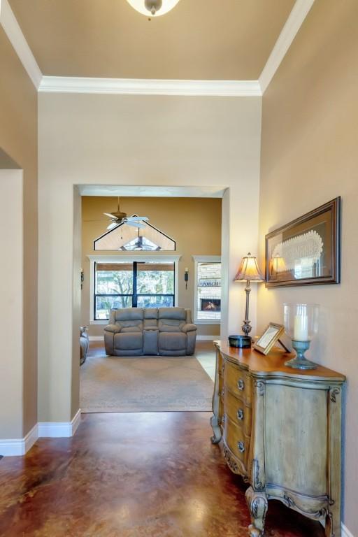 hallway featuring baseboards, a high ceiling, ornamental molding, and finished concrete floors