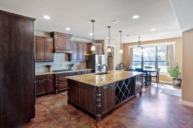 kitchen featuring visible vents, decorative backsplash, an island with sink, gas cooktop, and stainless steel fridge