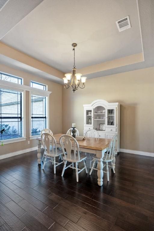 dining area with a tray ceiling, dark wood-style flooring, visible vents, and baseboards