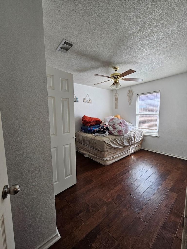 bedroom with a textured ceiling, hardwood / wood-style floors, visible vents, and a ceiling fan