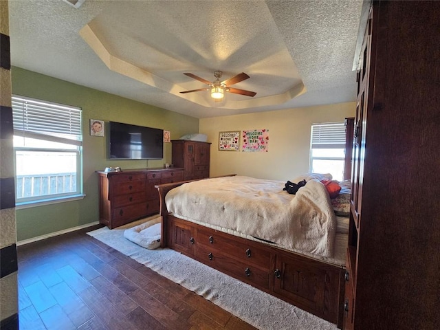 bedroom with dark wood-style floors, baseboards, a raised ceiling, and a textured ceiling