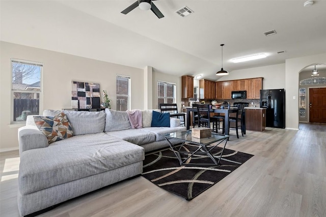 living area featuring arched walkways, light wood-type flooring, lofted ceiling, and visible vents