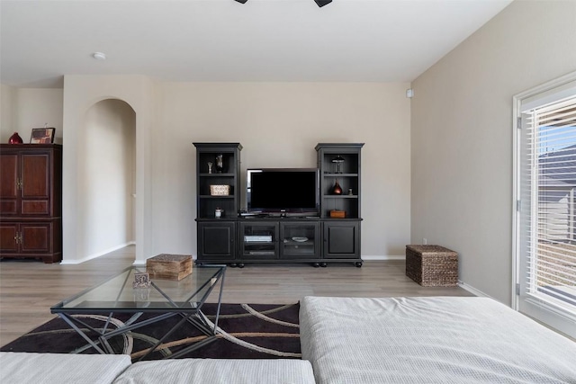 living room with light wood-type flooring, baseboards, and arched walkways