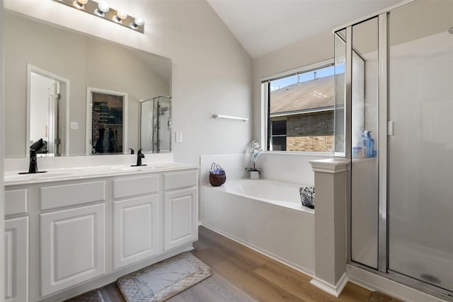 full bathroom featuring double vanity, lofted ceiling, wood finished floors, a shower stall, and a bath