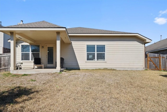 back of house featuring a shingled roof, a patio area, fence, and a lawn