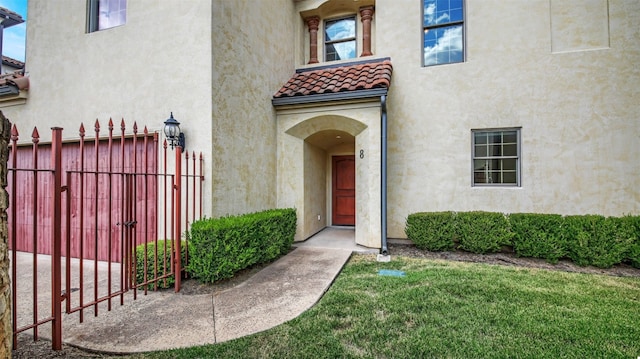 view of exterior entry with a tile roof, fence, a lawn, and stucco siding