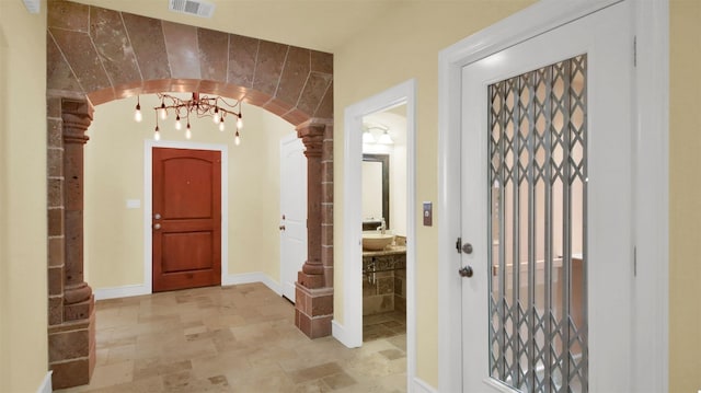 foyer entrance featuring arched walkways, baseboards, visible vents, and ornate columns