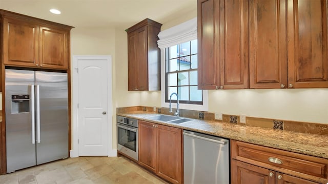 kitchen featuring light stone counters, recessed lighting, a sink, appliances with stainless steel finishes, and brown cabinetry