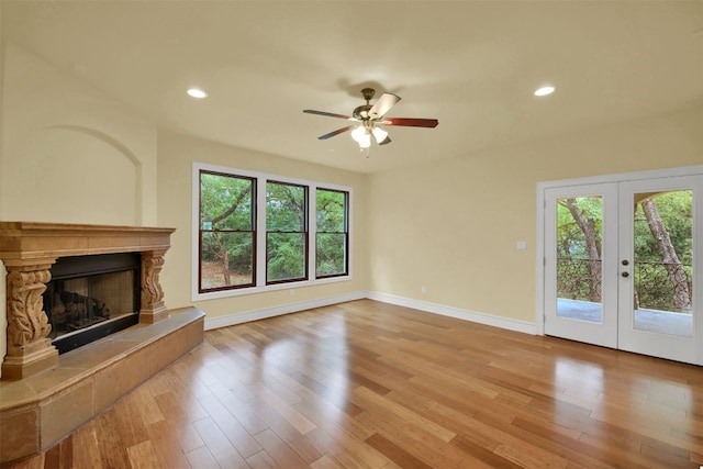 unfurnished living room with a healthy amount of sunlight, a fireplace with raised hearth, baseboards, and wood finished floors