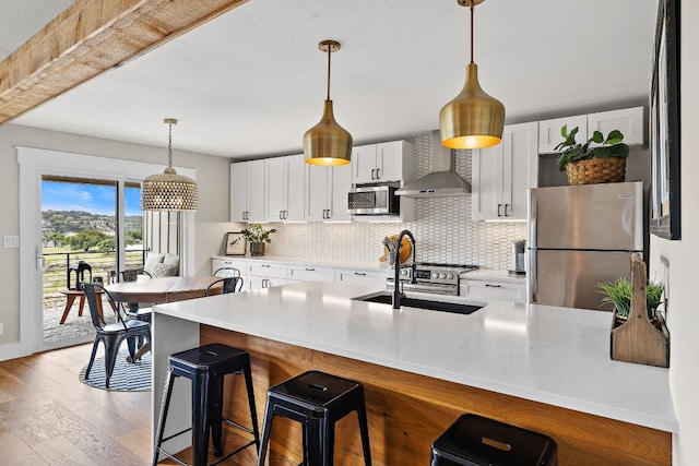 kitchen with backsplash, wall chimney exhaust hood, stainless steel appliances, and a sink