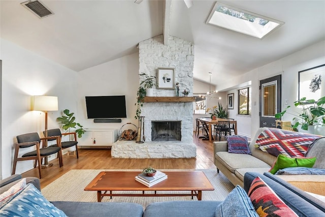 living room featuring vaulted ceiling with skylight, visible vents, a stone fireplace, and wood finished floors