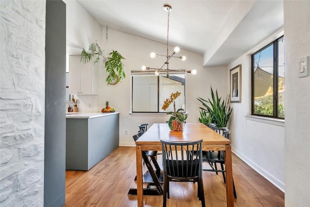 dining space with a chandelier, light wood-type flooring, lofted ceiling, and baseboards