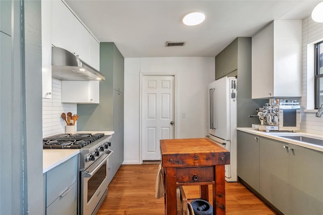 kitchen with a sink, visible vents, range hood, freestanding refrigerator, and high end range